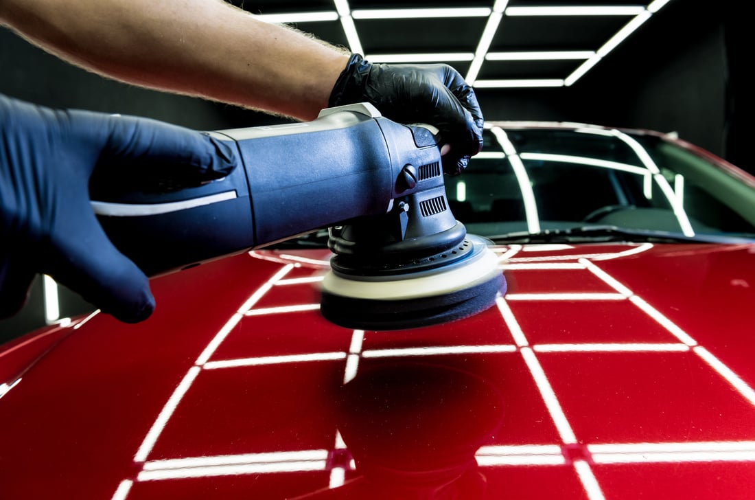 Car service worker polishes a car details with orbital polisher.